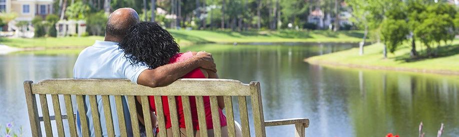 Man and woman sit on bench looking out over a pond