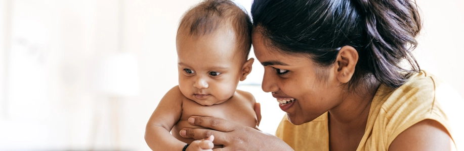 Young south Asian mother smiles and touches forehead to baby